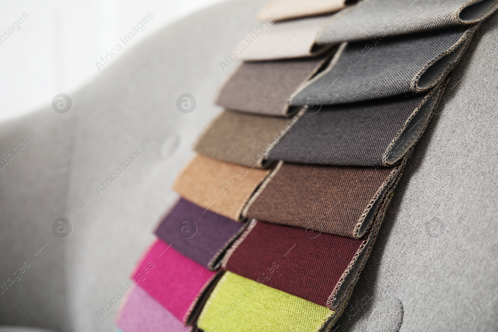 Photo of Catalog of colorful fabric samples on grey sofa, closeup. Space for text