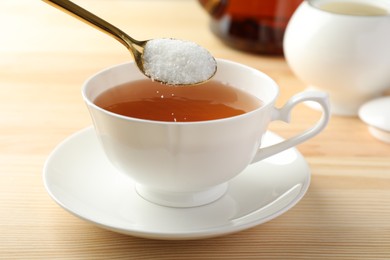 Photo of Adding sugar into cup of tea at wooden table, closeup
