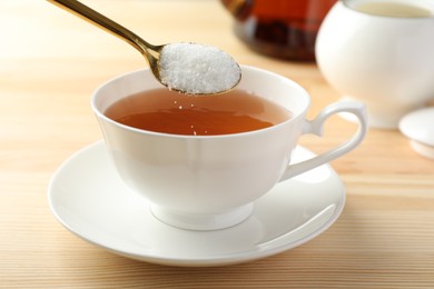 Adding sugar into cup of tea at wooden table, closeup