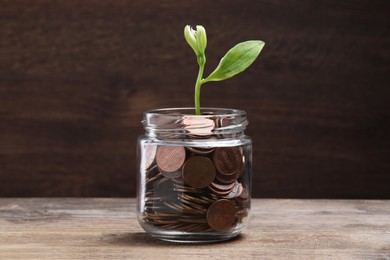 Glass jar with coins and flower on wooden table. Investment concept