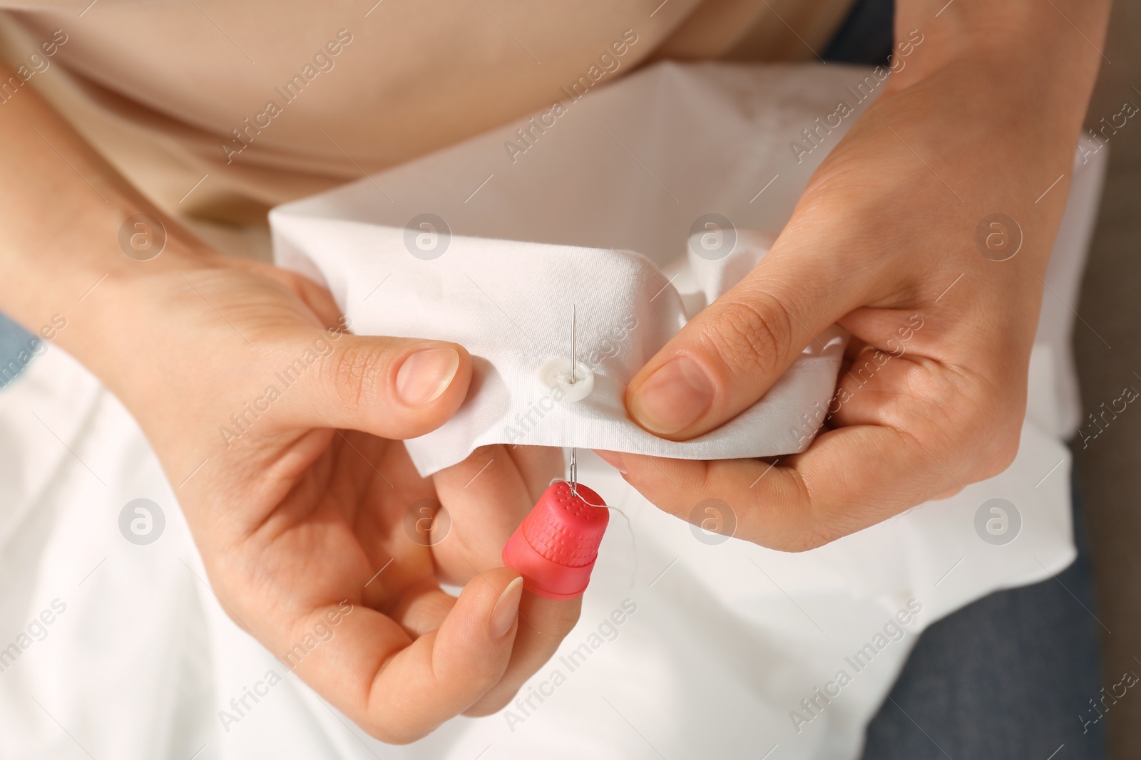 Photo of Woman sewing on white fabric with thimble and needle, above view