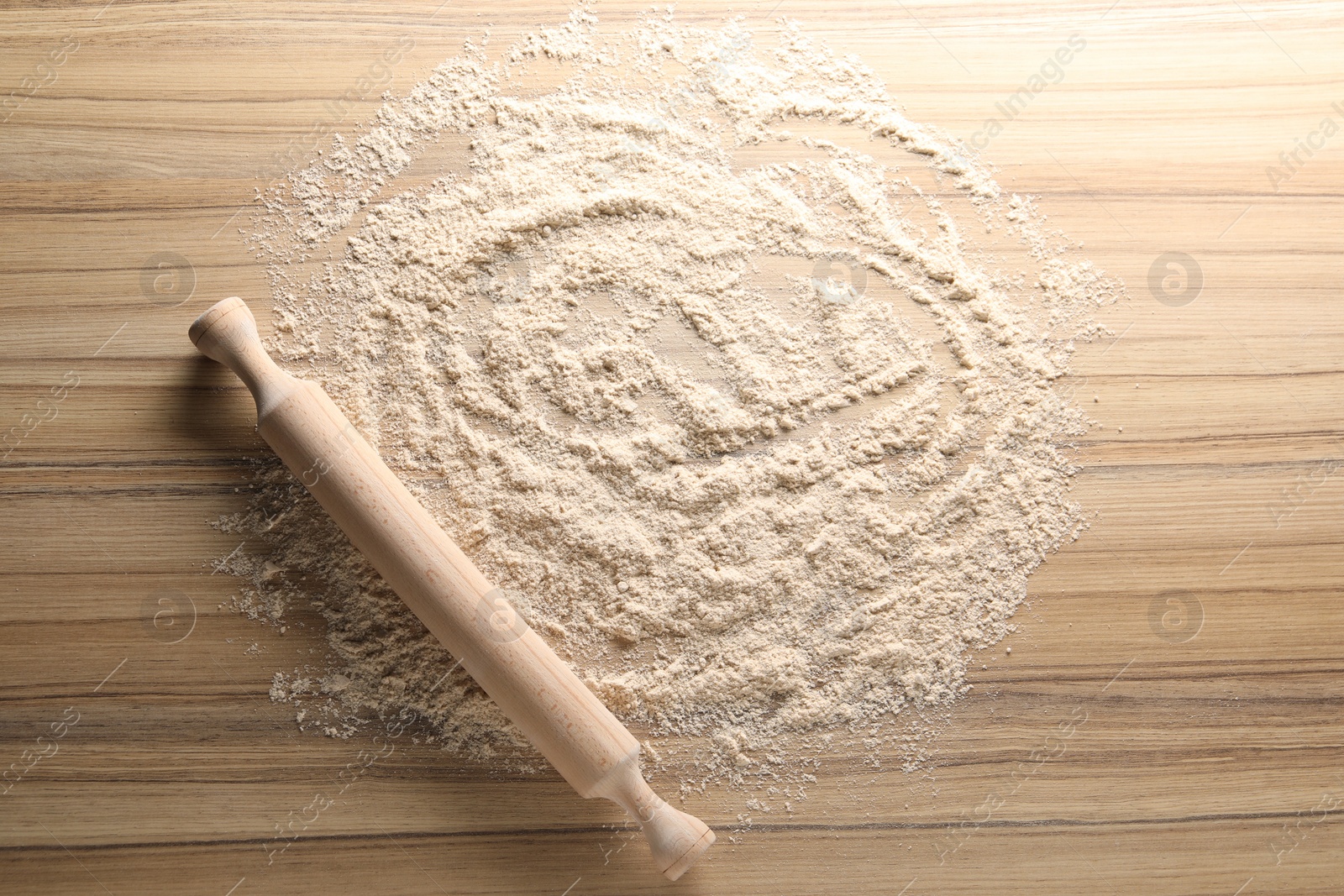 Photo of Scattered flour and rolling pin on wooden table, top view