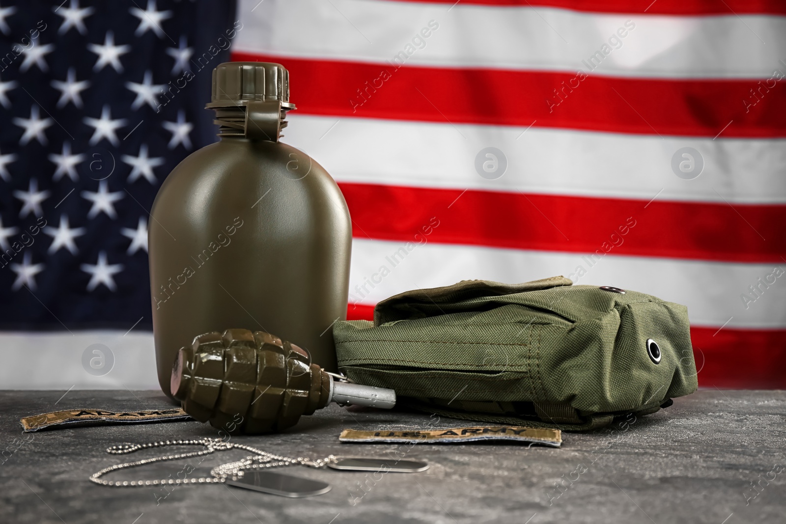 Photo of Military canteen, first-aid kit and grenade on table against American flag background