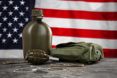 Military canteen, first-aid kit and grenade on table against American flag background