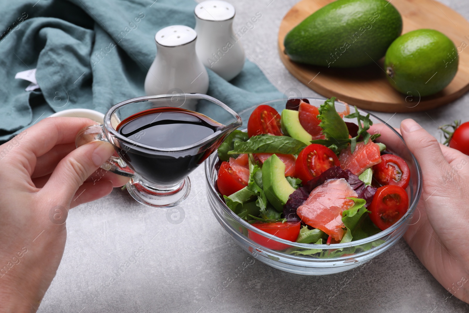 Photo of Woman adding soy sauce to tasty salad at grey table, closeup