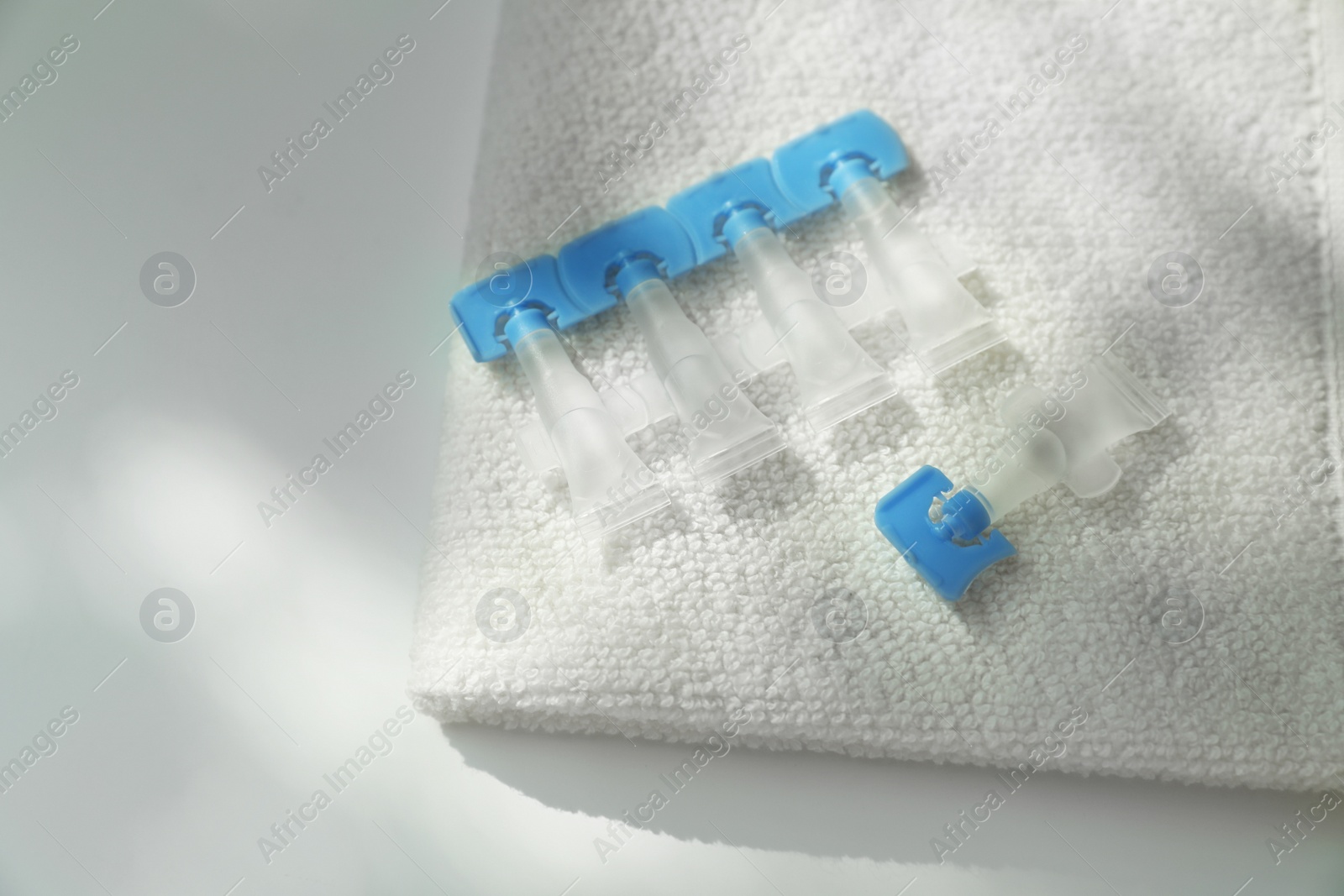 Photo of Single dose eye drops and towel on white table, closeup