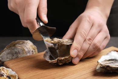 Photo of Man opening fresh oyster with knife at grey table, closeup