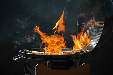 Photo of New modern barbecue grill with burning firewood on dark background
