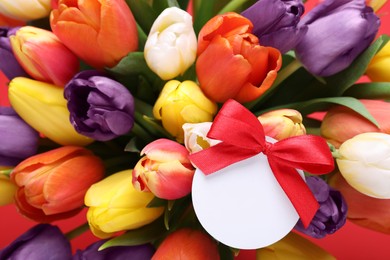 Photo of Bouquet of beautiful colorful tulips with blank card on red background, closeup. Birthday celebration