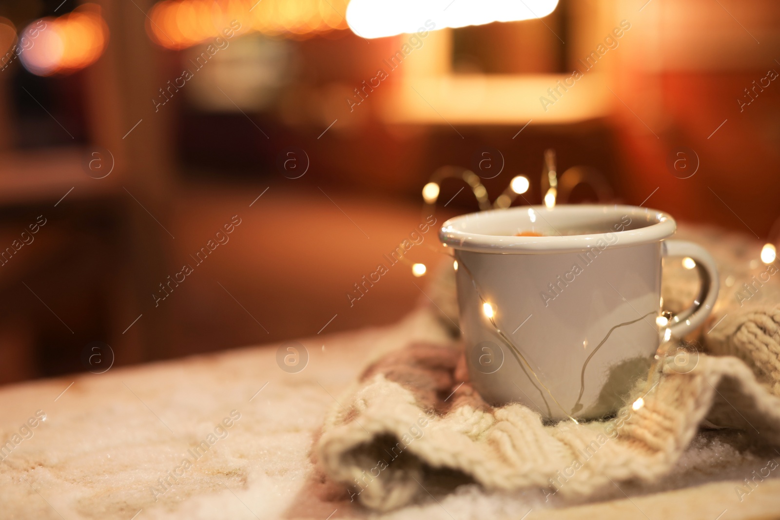 Photo of Cup of hot mulled wine and garland on table against blurred background. Space for text