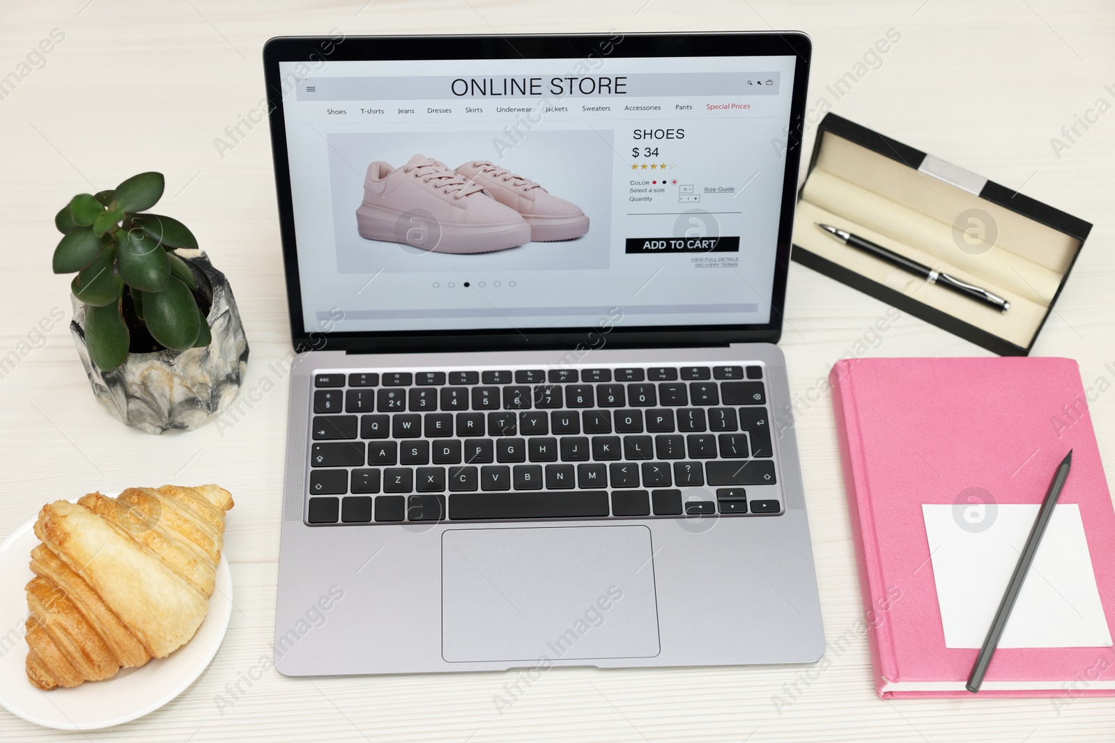 Photo of Online store. Laptop with open website, notebook, pen, croissant and pencil on wooden table, above view