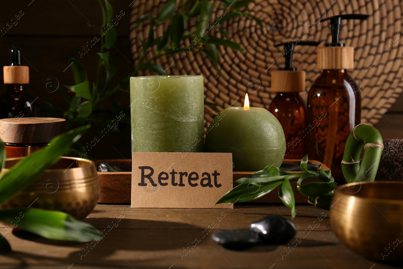 Photo of Card with word Retreat, green branches, cosmetic bottles and burning candles on wooden table