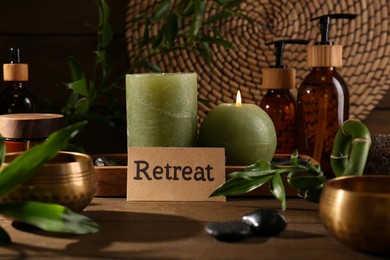 Card with word Retreat, green branches, cosmetic bottles and burning candles on wooden table