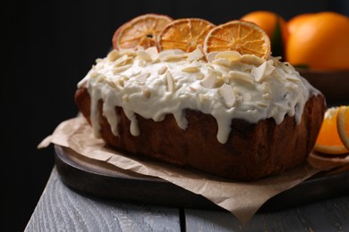 Photo of Delicious sweet cake with dry orange and almond petals on grey wooden table