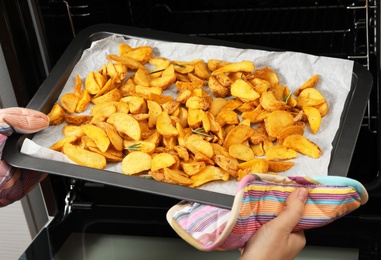 Photo of Woman taking hot roasted potatoes out of oven, closeup