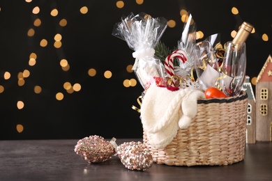 Wicker basket with Christmas gift set on grey table against festive lights. Space for text
