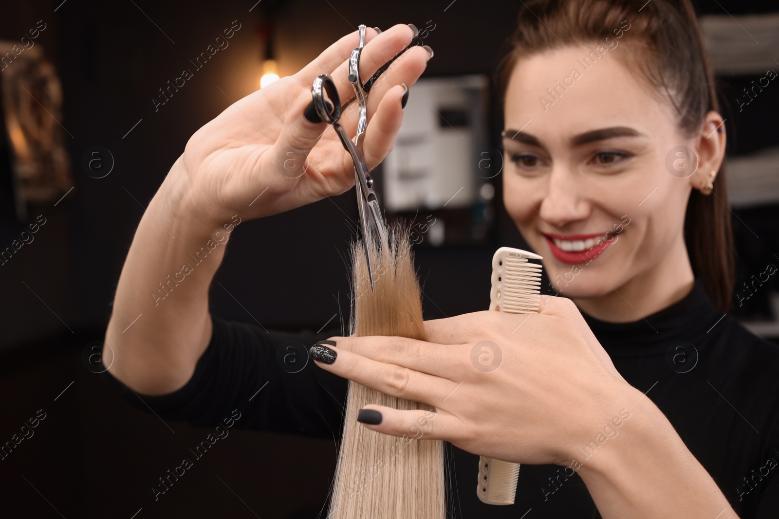 Photo of Professional hairdresser cutting woman's hair in salon, focus on hands
