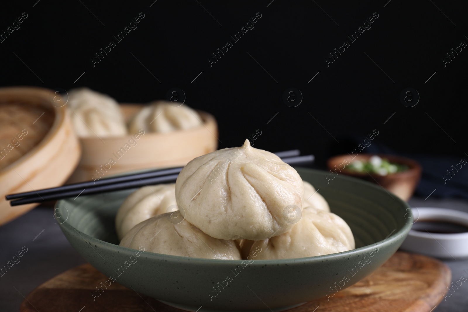 Photo of Delicious bao buns (baozi) in bowl and chopsticks on grey table, closeup