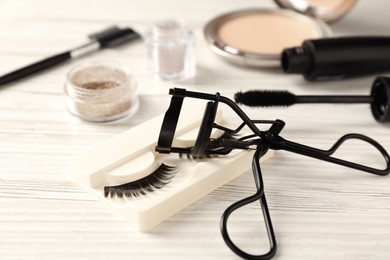 Photo of False eyelashes and curler on white wooden table, closeup