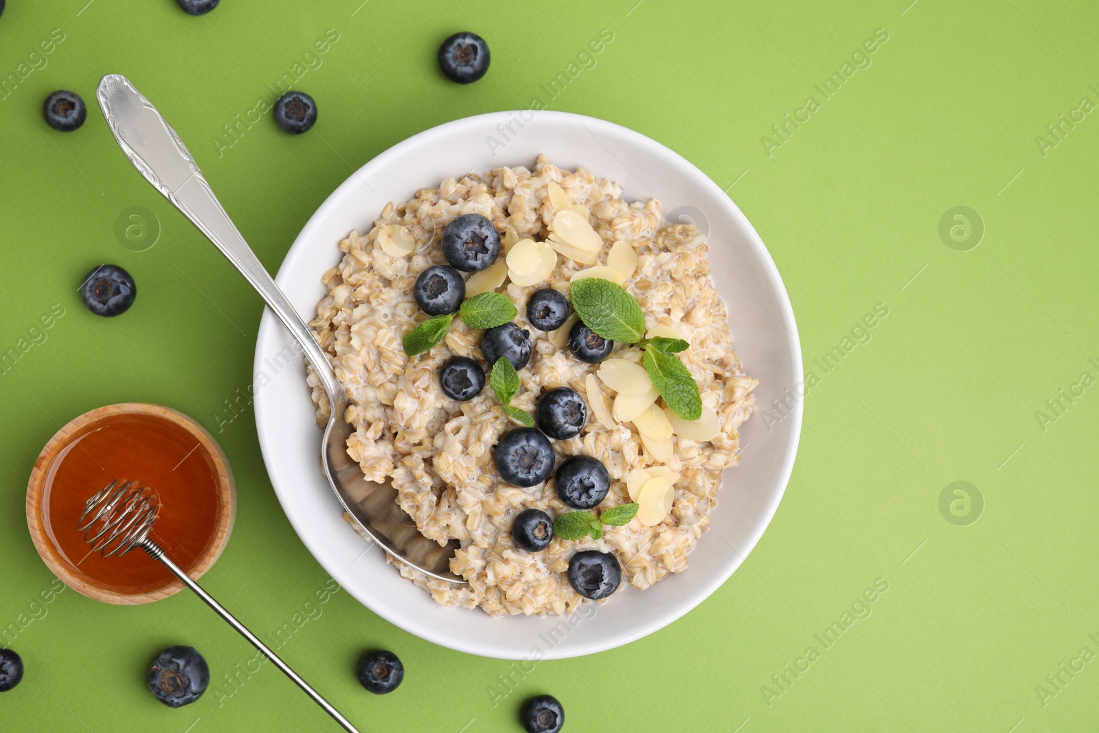 Photo of Tasty oatmeal with blueberries, mint and almond petals in bowl on light green background, flat lay