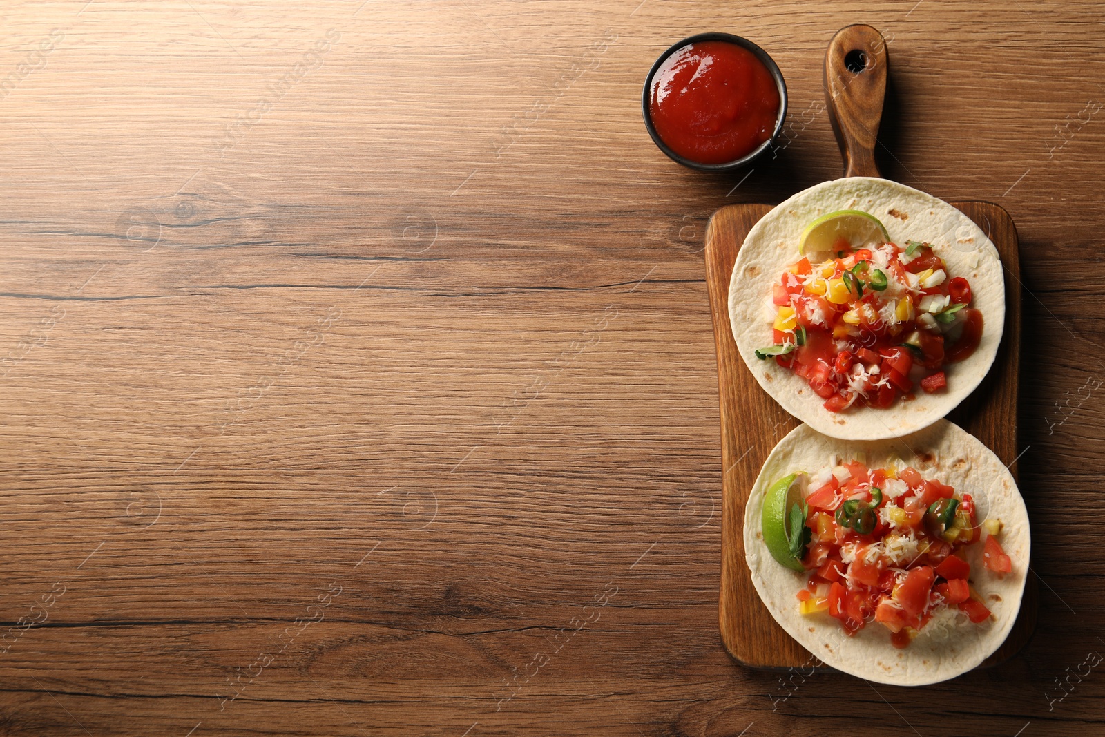 Photo of Delicious tacos with vegetables, lime and ketchup on wooden table, top view. Space for text