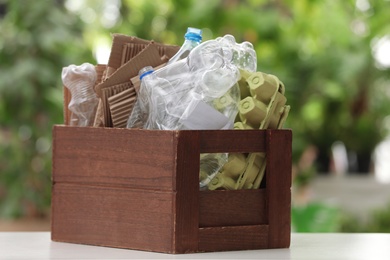 Photo of Wooden crate with different garbage on blurred background. Waste recycling concept