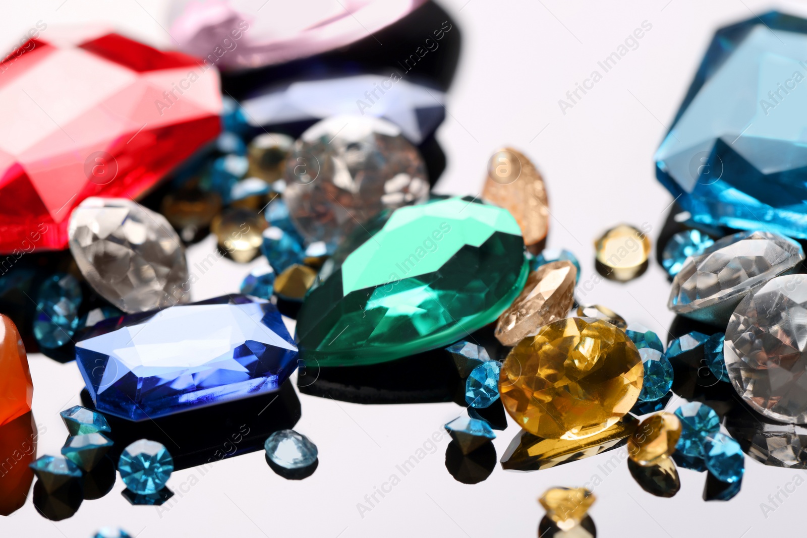 Photo of Different beautiful gemstones for jewelry on mirror surface, closeup