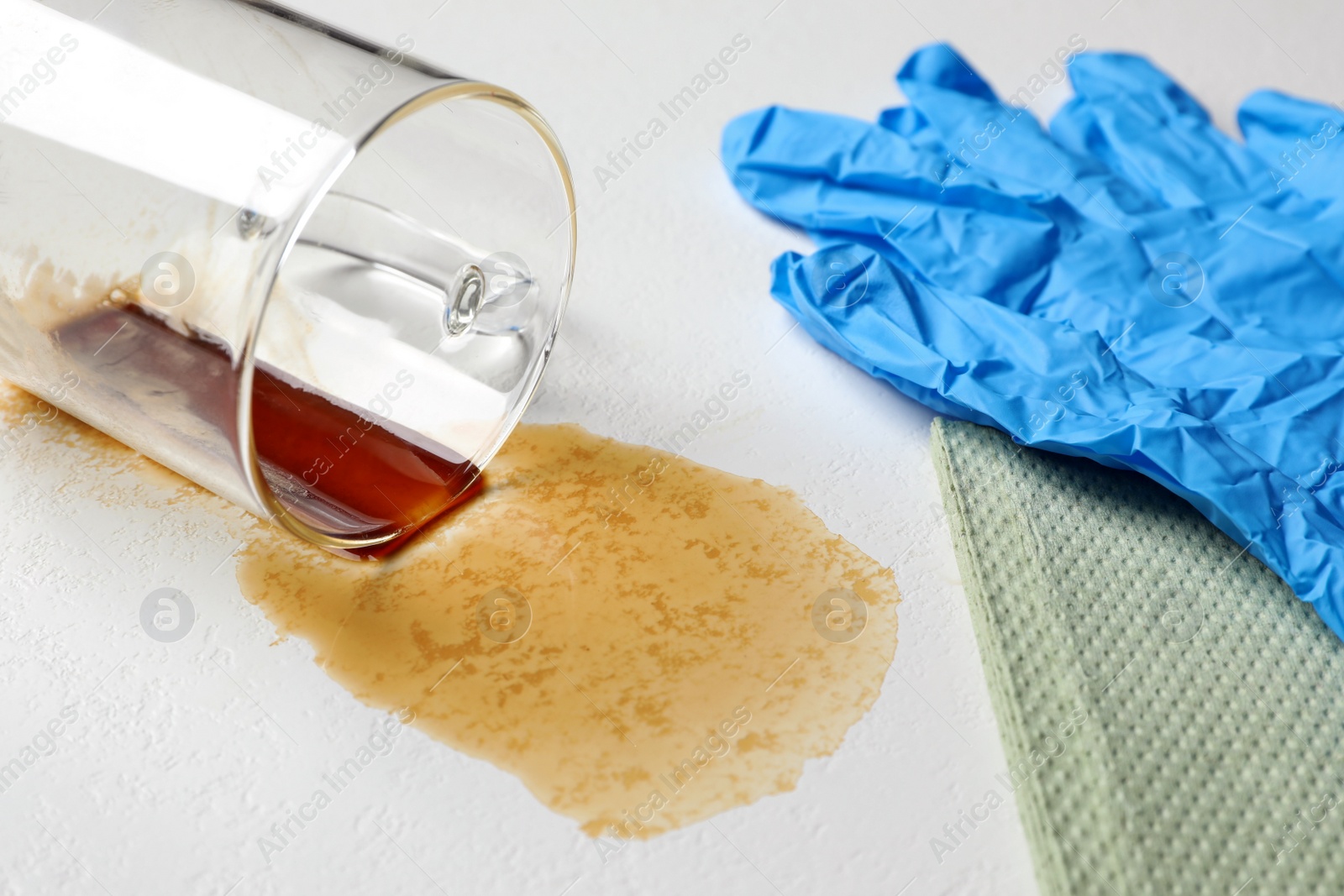 Photo of Glove, paper towel, overturned cup and spilled coffee on light table, closeup