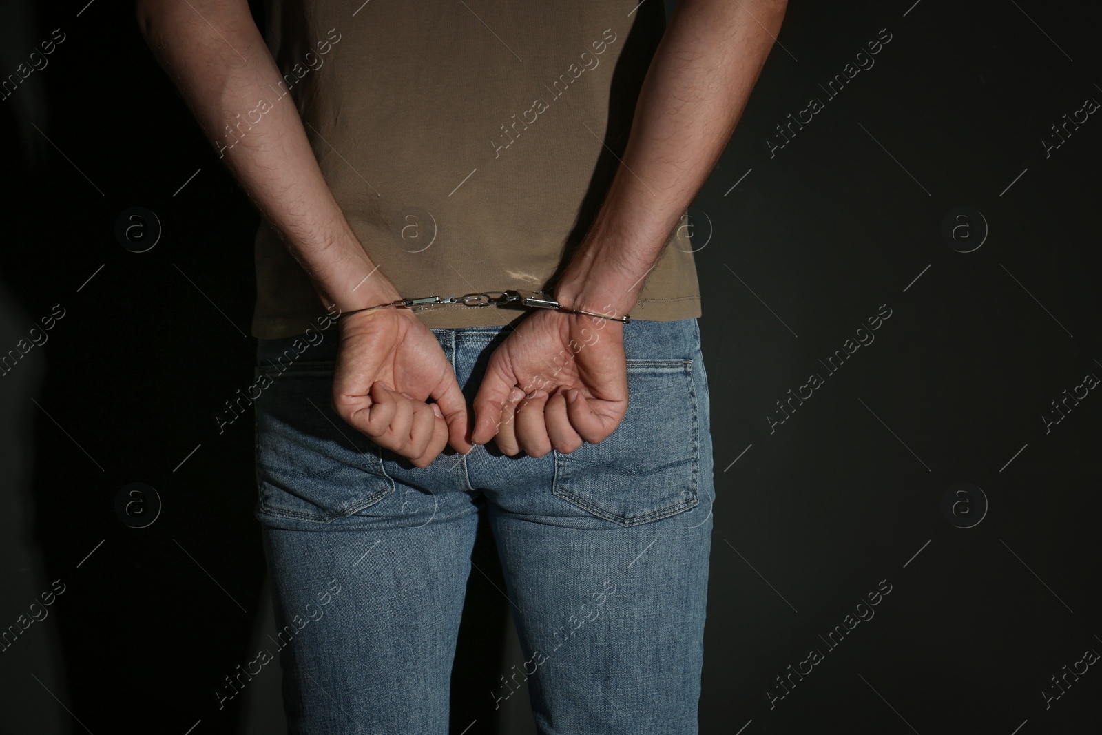 Photo of Male criminal in handcuffs near black wall, closeup