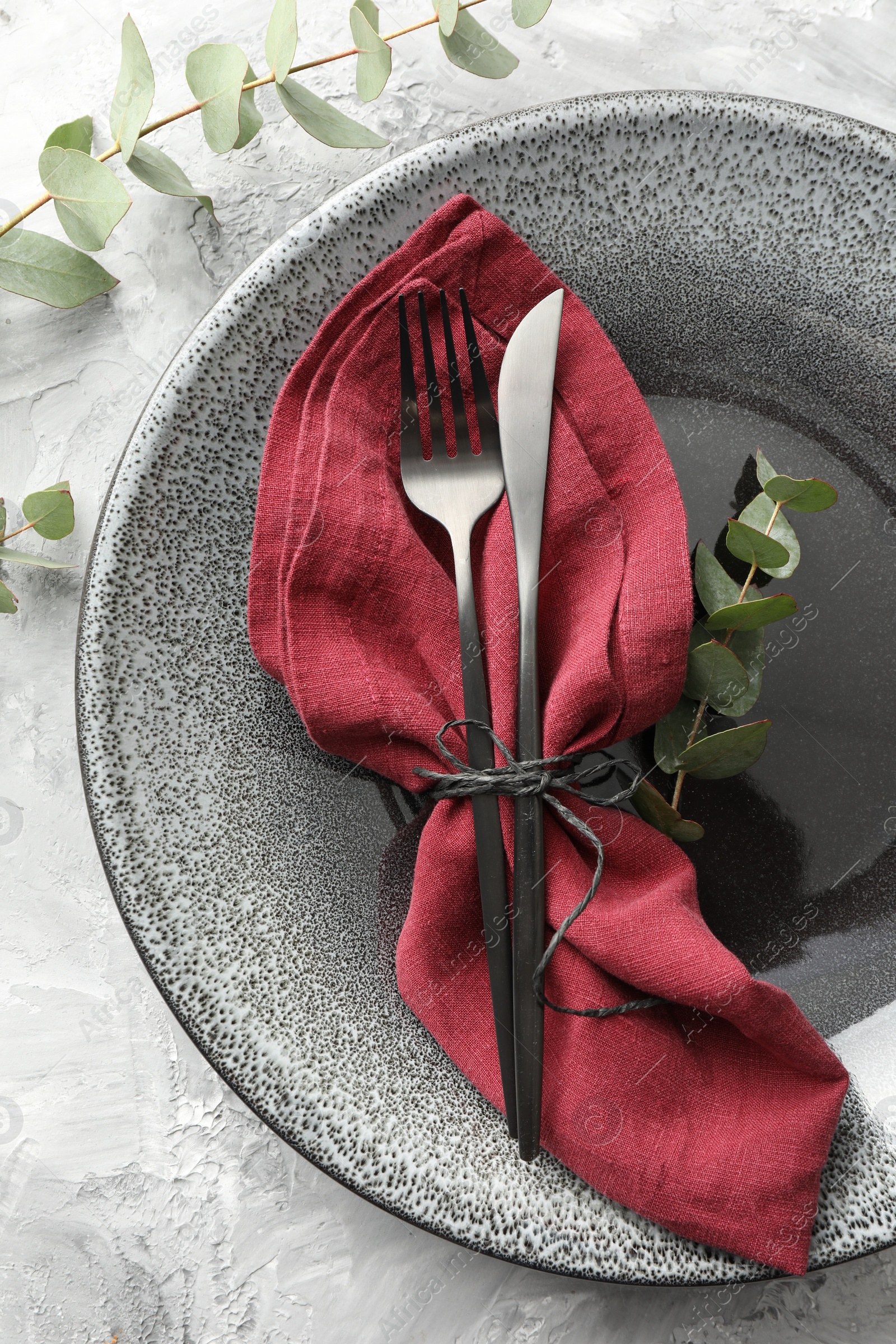 Photo of Stylish setting with cutlery, napkin, eucalyptus branches and plate on grey textured table, top view