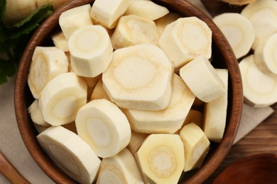 Photo of Cut fresh ripe parsnip in bowl on wooden table, top view