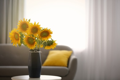 Photo of Vase with beautiful yellow sunflowers on table in room, space for text