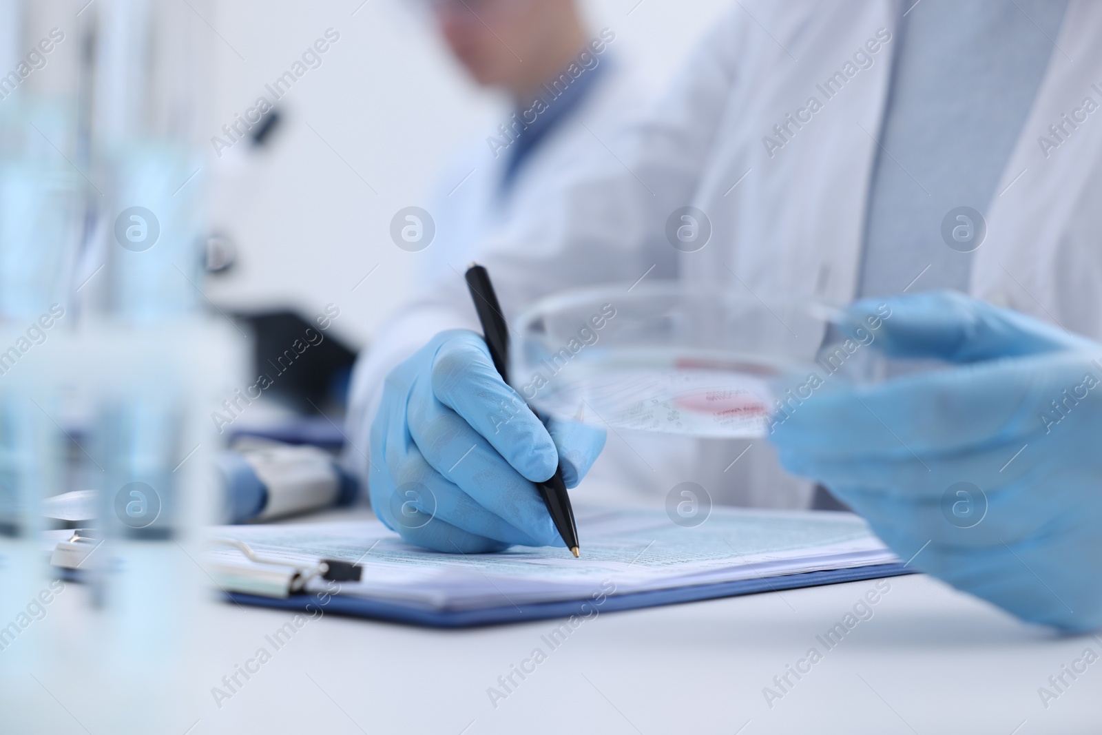 Photo of Laboratory worker holding petri dish with blood sample while working at white table, closeup