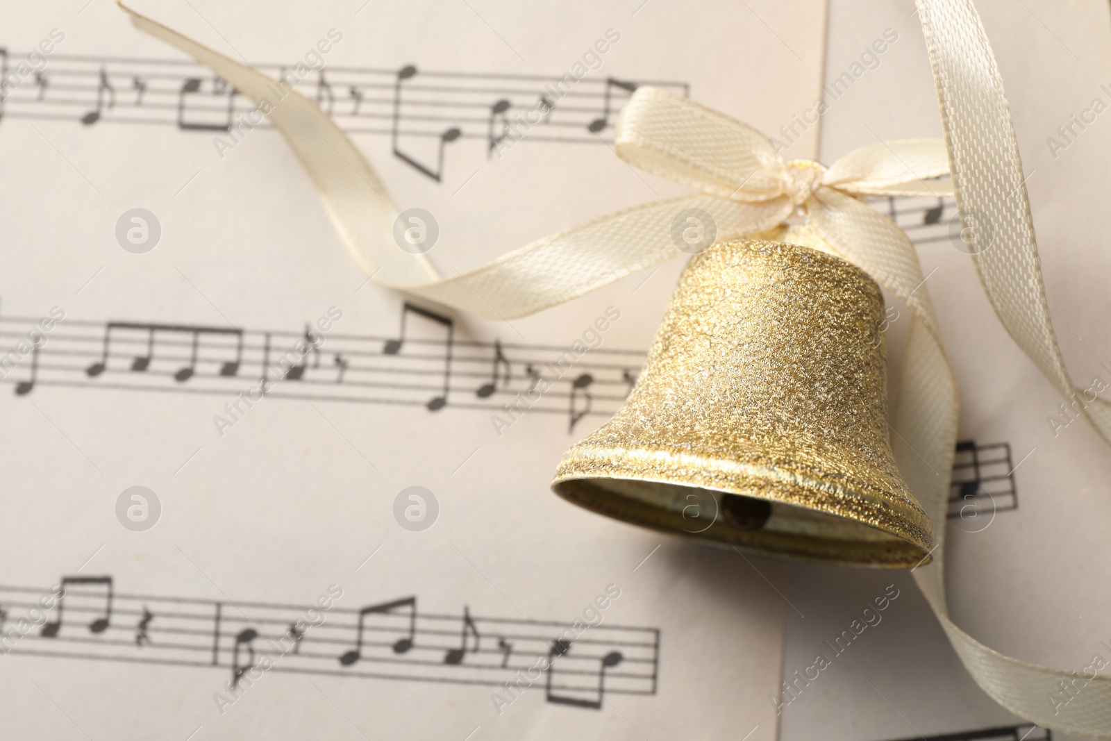 Photo of Golden shiny bell with bow on music sheet, top view. Space for text. Christmas decoration