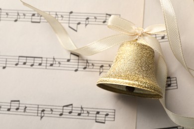 Golden shiny bell with bow on music sheet, top view. Space for text. Christmas decoration