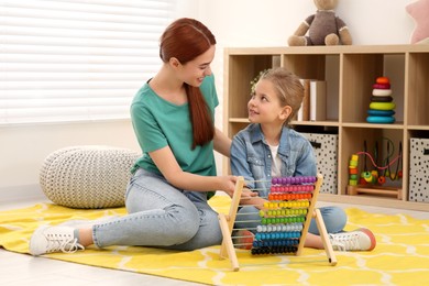 Happy mother and daughter playing with abacus on floor in room. Learning mathematics with fun