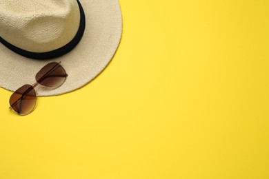 Hat and sunglasses on yellow background, flat lay with space for text. Sun protection