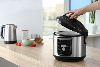 Young woman using modern multi cooker in kitchen. Space for text