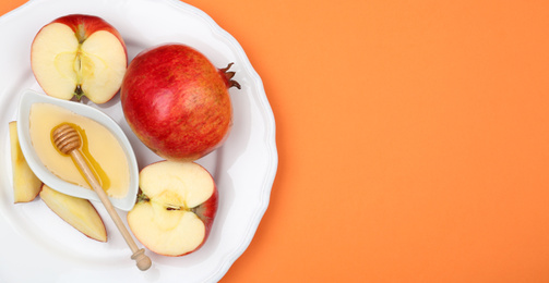 Photo of Honey, apples and pomegranate on orange background, top view. with space for text Rosh Hashanah holiday