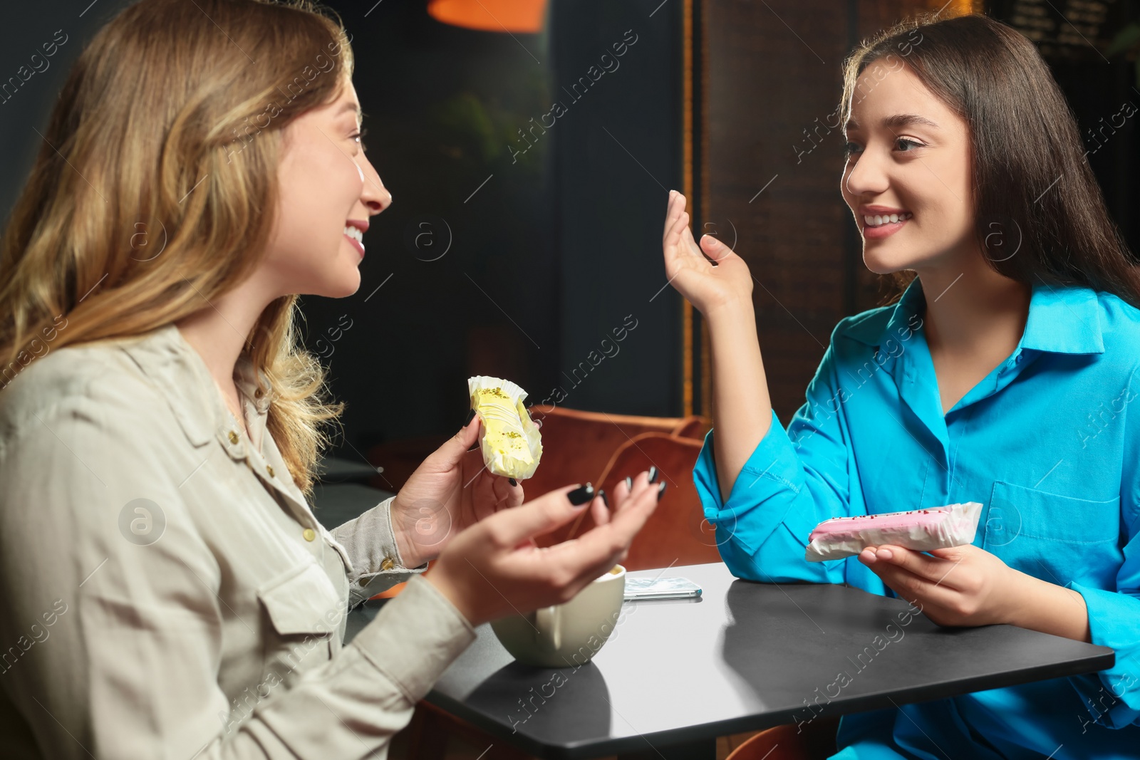 Photo of Young women with coffee and eclairs spending time together in cafe