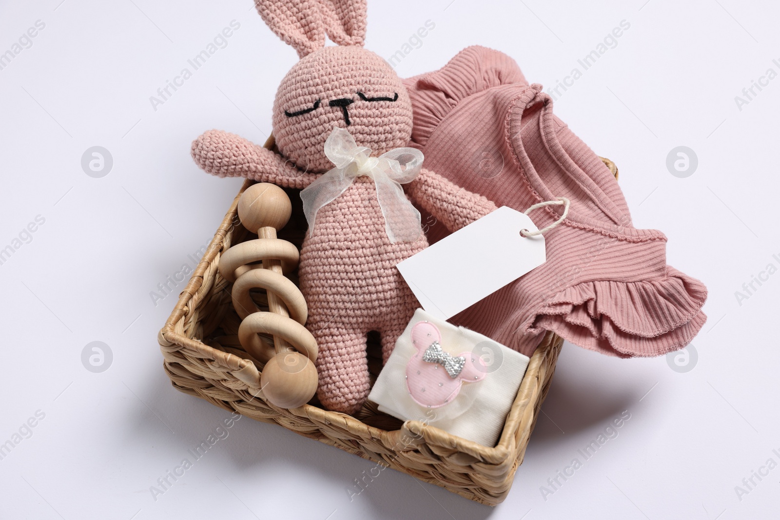 Photo of Different baby accessories, clothes and blank card in wicker box on white background