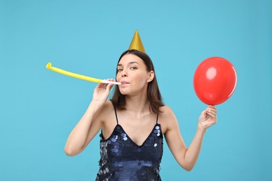 Young woman in party hat with blower on light blue background