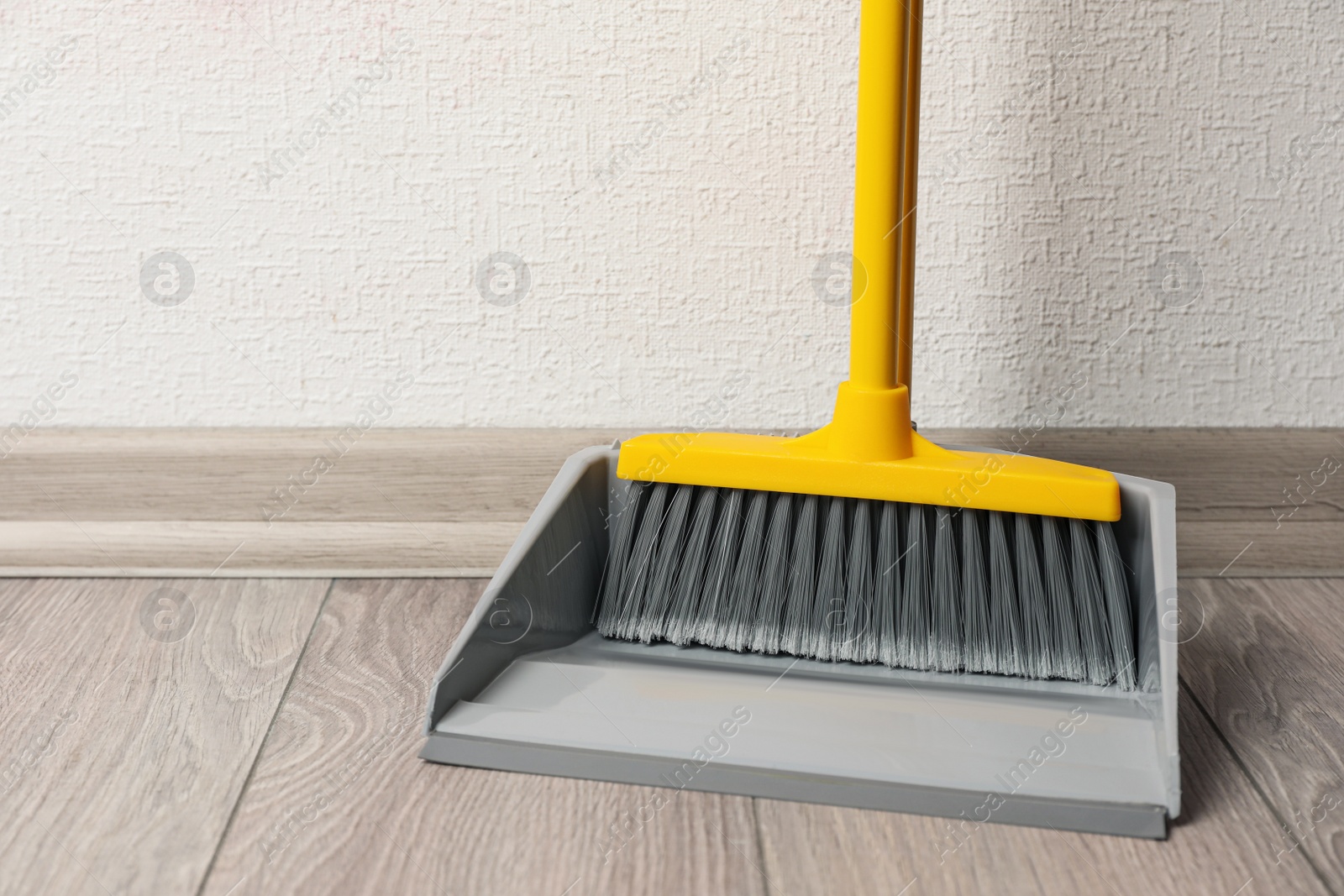 Photo of Plastic broom with dustpan on wooden floor indoors