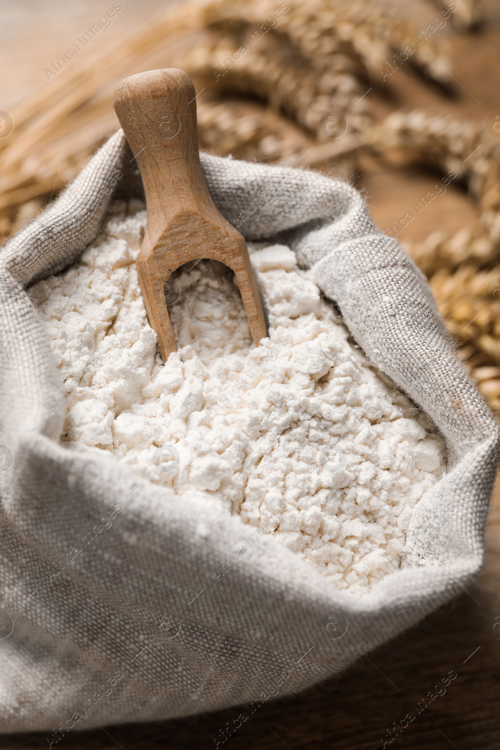 Photo of Wheat flour and wooden scoop in sack bag on table, closeup