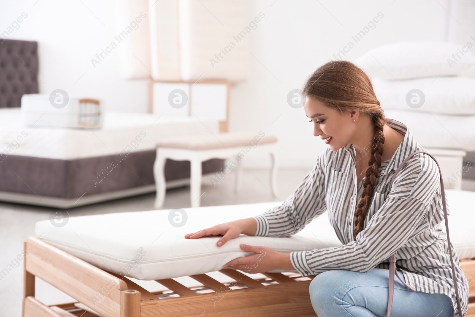 Photo of Young woman touching mattress in furniture store. Space for text