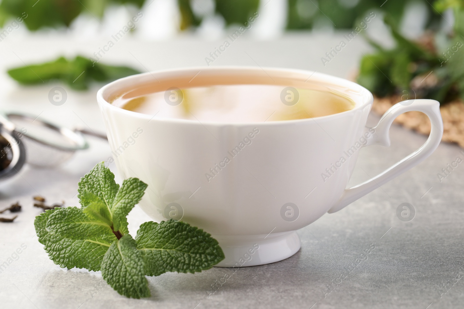 Photo of Cup of aromatic green tea with fresh mint on grey table, closeup