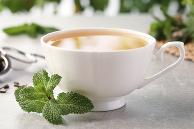 Cup of aromatic green tea with fresh mint on grey table, closeup