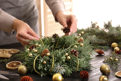 Photo of Florist making beautiful Christmas wreath at black wooden table indoors, closeup
