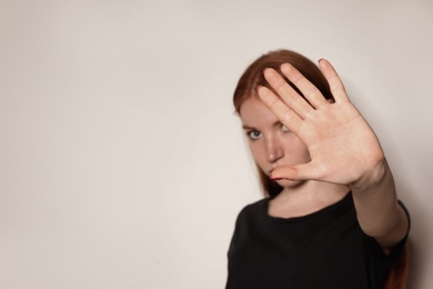 Young woman making stop gesture against light background, focus on hand. Space for text