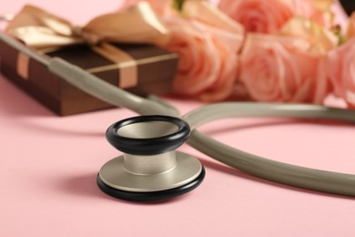 Photo of Stethoscope, gift box and flowers on pink background, closeup. Happy Doctor's Day